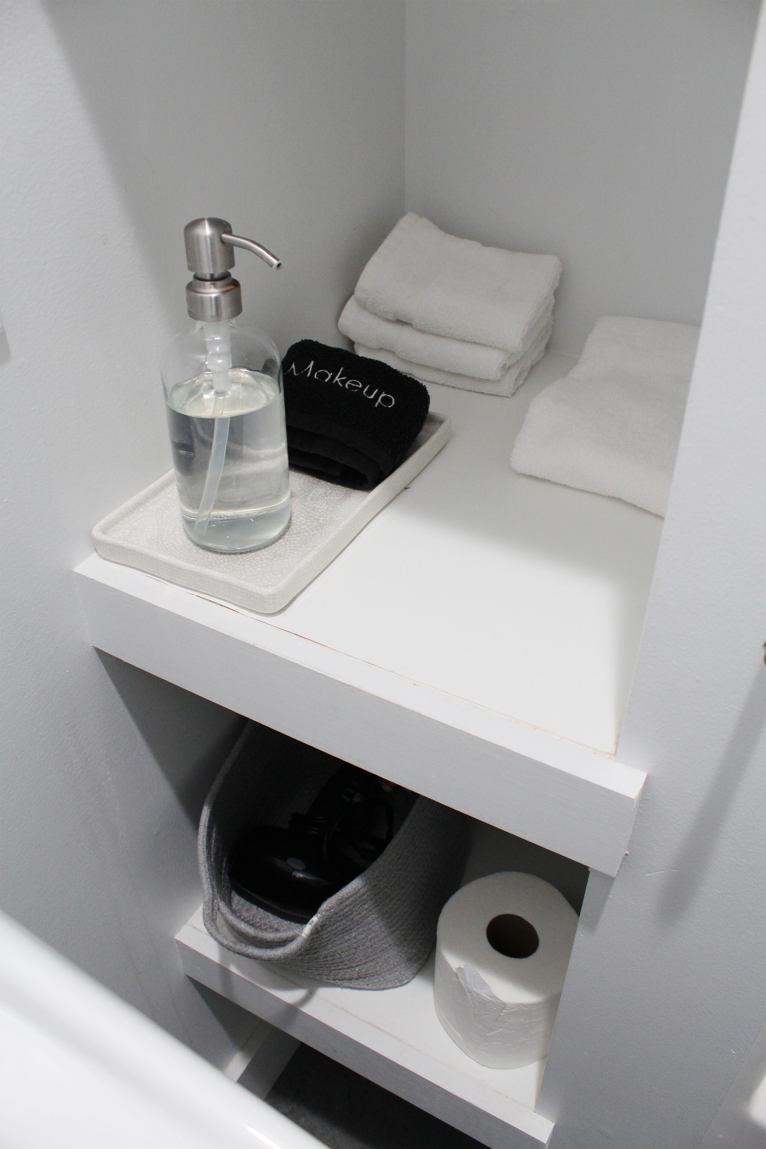 Ein Badezimmerschrank mit einer Seifenflasche, einem schwarzen Verschluss und einem Stapel weißer Handtücher.