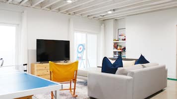 Un salon avec une table de ping-pong, un canapé, un téléviseur et une cible accrochée au mur.