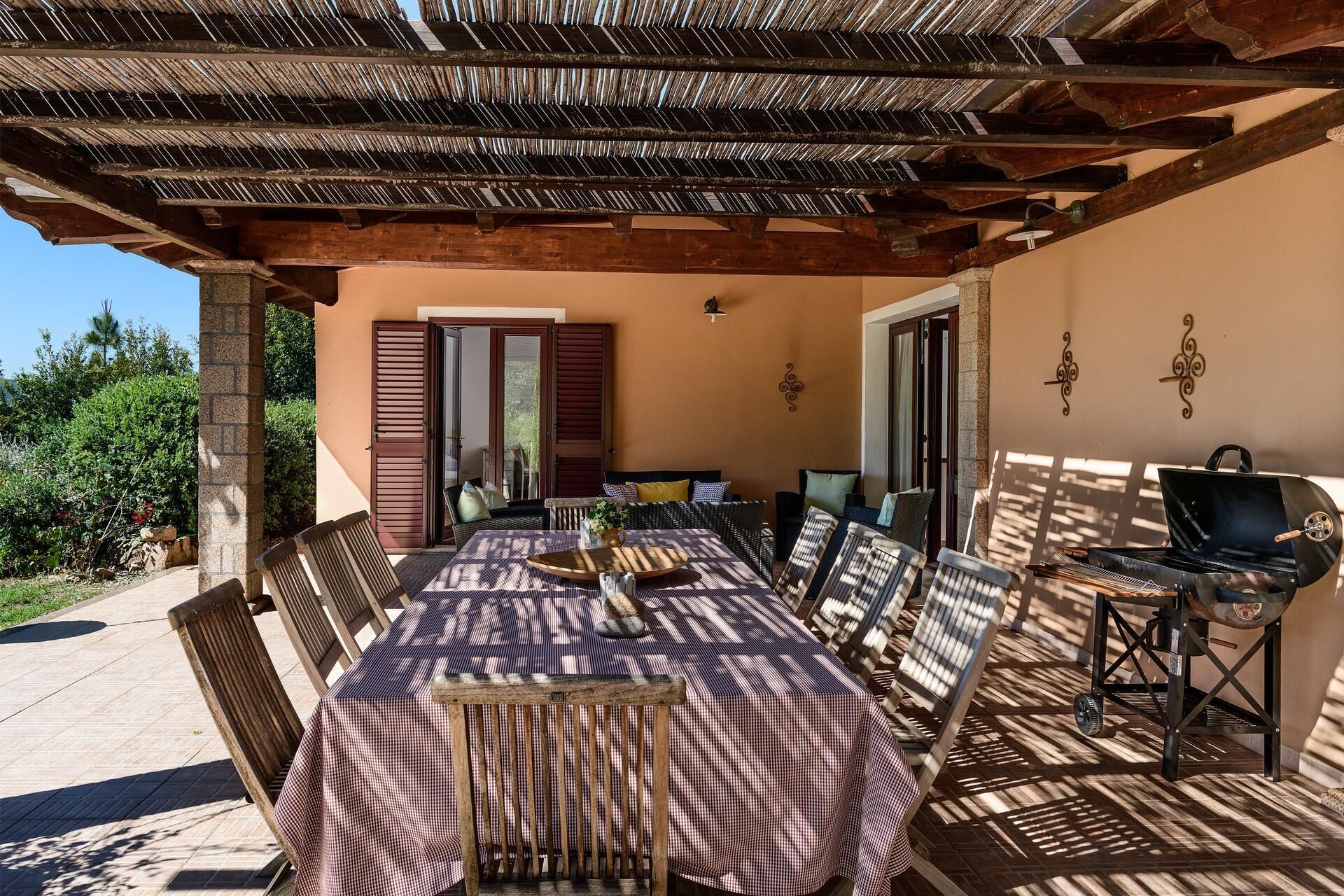 An outdoor patio with a table and chairs, a grill, and a covered area with wooden beams.