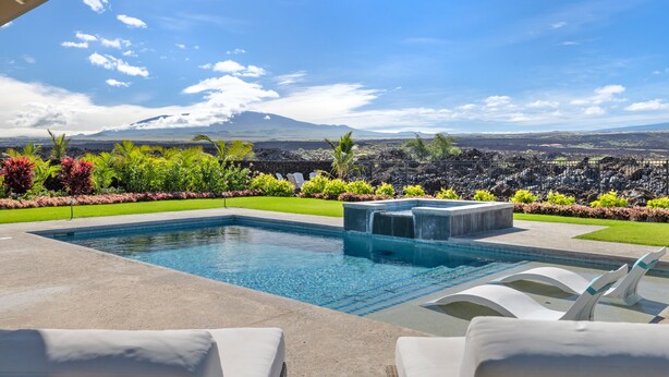 A pool with a waterfall feature, surrounded by lush greenery and a view of a distant mountain range. - 3 Bedroom Private Home at Waikoloa Beach with Pool (Waikoloa)