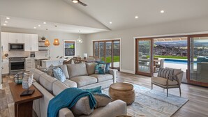 A modern living space with a kitchen, dining area, and a large sliding glass door leading to a pool. - 3 Bedroom Private Home at Waikoloa Beach with Pool (Waikoloa)