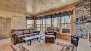 A cozy log cabin interior with a wooden ceiling, a stone wall, and a large window. - Cozy, Luxurious Fox Den in the Shenandoah Valley (Luray)