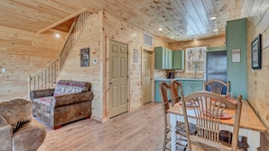 A wooden interior with a staircase, a sofa, a dining table with chairs, and a kitchen area with green cabinets. - Cozy, Luxurious Fox Den in the Shenandoah Valley (Luray)