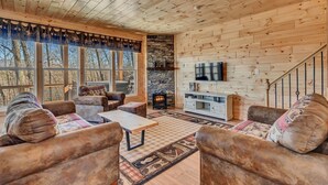 A cozy living room with wooden walls, a stone fireplace, a TV, and a staircase. - Cozy, Luxurious Fox Den in the Shenandoah Valley (Luray)