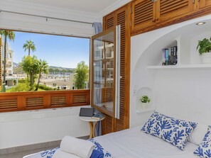 A bedroom with a view of a beach, a small table with a laptop, and a bookshelf with books. - Apartamento Carabela 51· 2 bedrooms · 3 beds · 1 bath (Puerto de Alcudia)