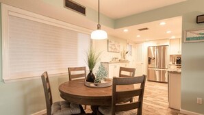 A dining area with a round wooden table, four chairs, a vase with greenery, and a pendant light. - Beautiful Hutchinson Island Condo - Steps to Ocean (Fort Pierce)