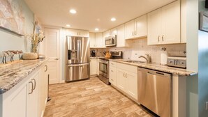 A modern kitchen with stainless steel appliances, white cabinetry, and a marble countertop. - Beautiful Hutchinson Island Condo - Steps to Ocean (Fort Pierce)