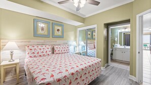 Ein Schlafzimmer mit Bett, Nachttischen, Deckenventilator und einem durchgegangenen Tür erkennbaren Badezimmer.