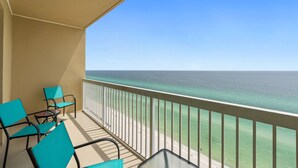 Ein Balkon mit türkisfarbenen Stühlen und einem Glastisch, der auf einen Strand und den Ozean blickt.