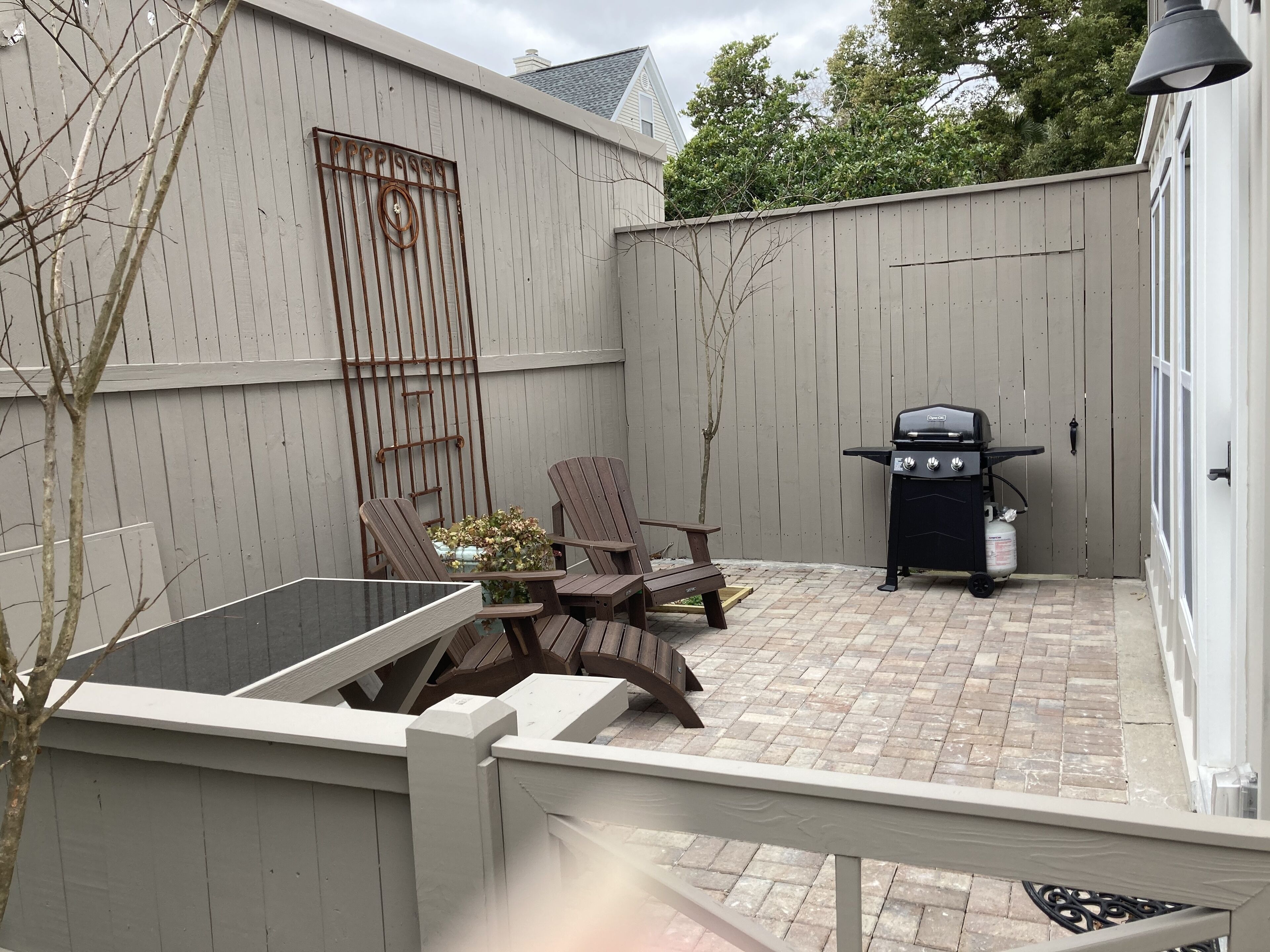 A patio with a grill, two Adirondack chairs, and a table.
