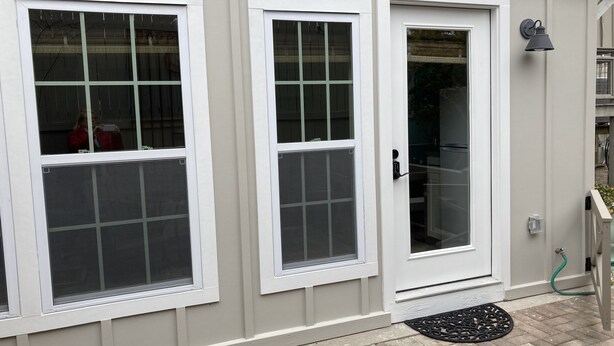 A building with three white-framed windows, a door, and a small outdoor area with a doormat and a hose. - Beach Walk Bungalow 1Bedroom 1Bath, 4 blocks to the beach!! Private Courtyard (St. Simons Island)