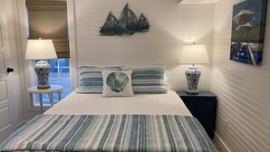 A bedroom with a bed, two nightstands, two lamps, a painting, and a view of the outside. - Beach Walk Bungalow 1Bedroom 1Bath, 4 blocks to the beach!! Private Courtyard (St. Simons Island)