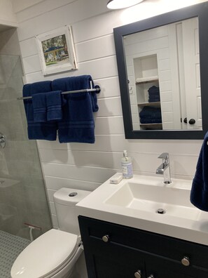 Une salle de bain avec des toilettes blanches, un lavabo surmonté d’un miroir et un porte-serviettes avec des serviettes bleues.