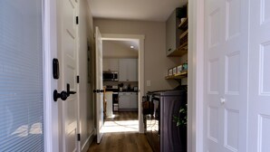 Um corredor com piso de madeira, portas brancas e uma cozinha visível ao fundo.