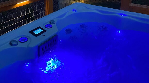 Uma banheira de hidromassagem com iluminação azul, um deck de madeira e uma casa ao fundo.