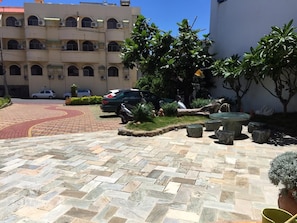 A courtyard with a paved walkway, outdoor seating, and parked cars. - Brittany Hotel (Hengchun)