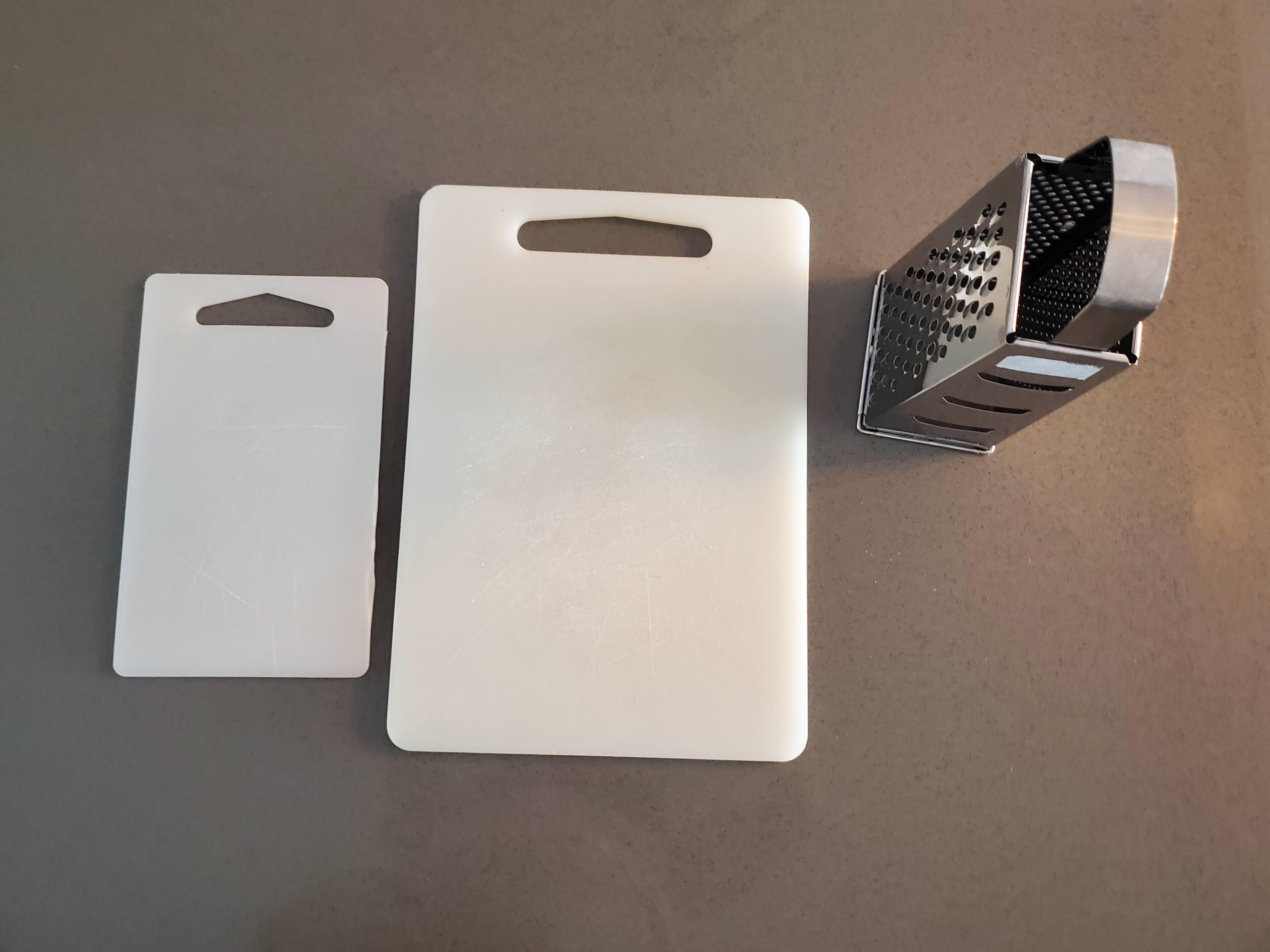 Deux planches à découper blanches et une râpe en métal sur un plan de travail.