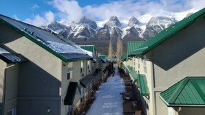 Un pasillo con suelo cubierto de nieve, edificios con techos verdes y montañas nevadas al fondo.