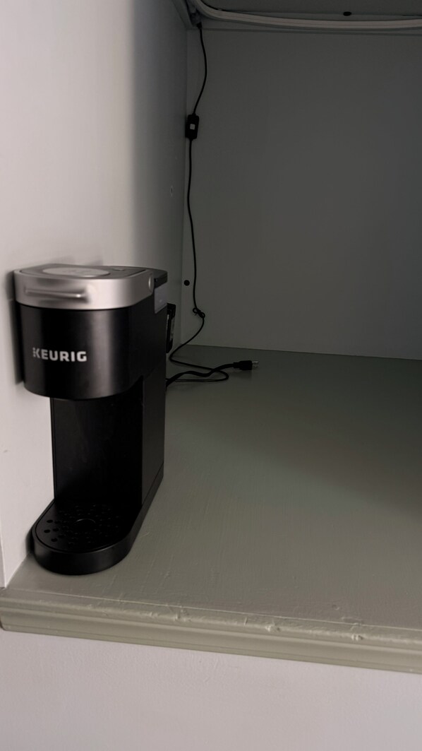 A Keurig coffee maker on a white countertop with a power cord plugged in.