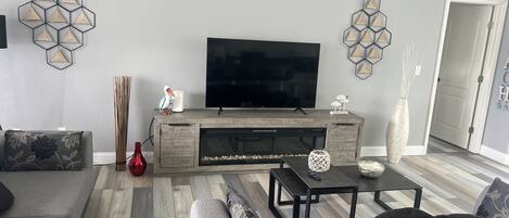Un saló modern amb un sofà gris, una taula de centre i un televisor sobre un moble de roba de fusta.