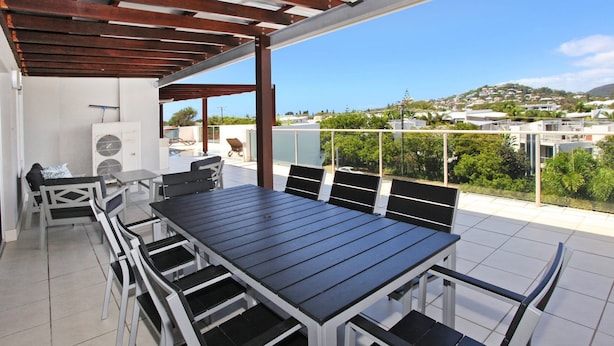 Eine überdachte Terrasse mit Tisch und Stühlen, ein Pool und Blick auf eine Wohngegend.