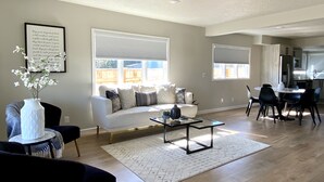 Una sala de estar moderna con un sofá blanco, una mesa de centro de vidrio y un comedor con una cocina al fondo.