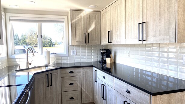 Cocina moderna con armarios de madera clara, encimeras negras y un amplio ventanal que proporciona luz natural.
