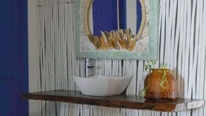 Un bany amb una prestatgeria de fusta que sosté un lavabo blanc i un ramó decoratiu.