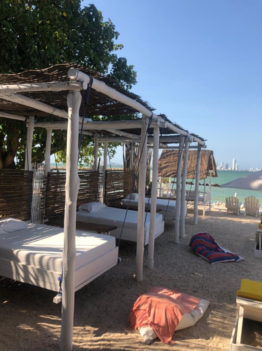 Eine Strandhütte mit strohgedecktem Dach, weißen Liegestühlen und sandigem Untergrund.