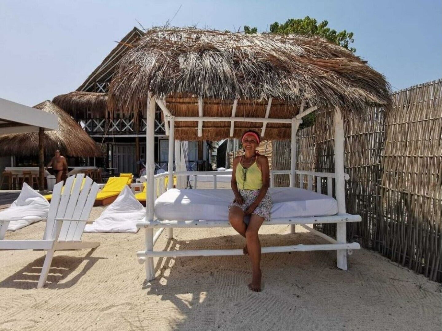 Een strandhut met rieten dak, witte loungesteunen en een zandstrand.