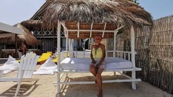 Een strandhut met rieten dak, witte loungesteunen en een zandstrand.