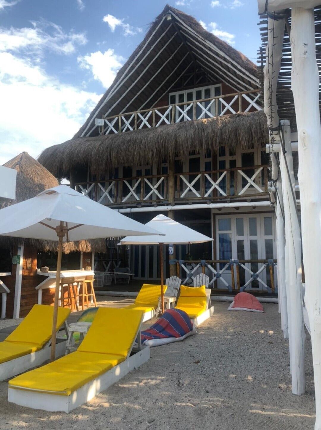 Ein Gebäude am Strand mit einem Reetdach, Außenbestuhlung und einem Sandbereich mit Liegestühlen.