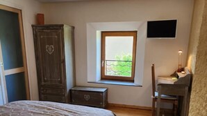 A bedroom with a bed, a desk, a chair, a wardrobe, a window, and a wall-mounted TV. - Chez la Lise - TANCON (TANCON)