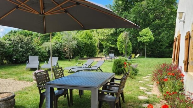 A patio with a table and chairs, a large umbrella, and a garden with red flowers. - Chez la Lise - TANCON (TANCON)