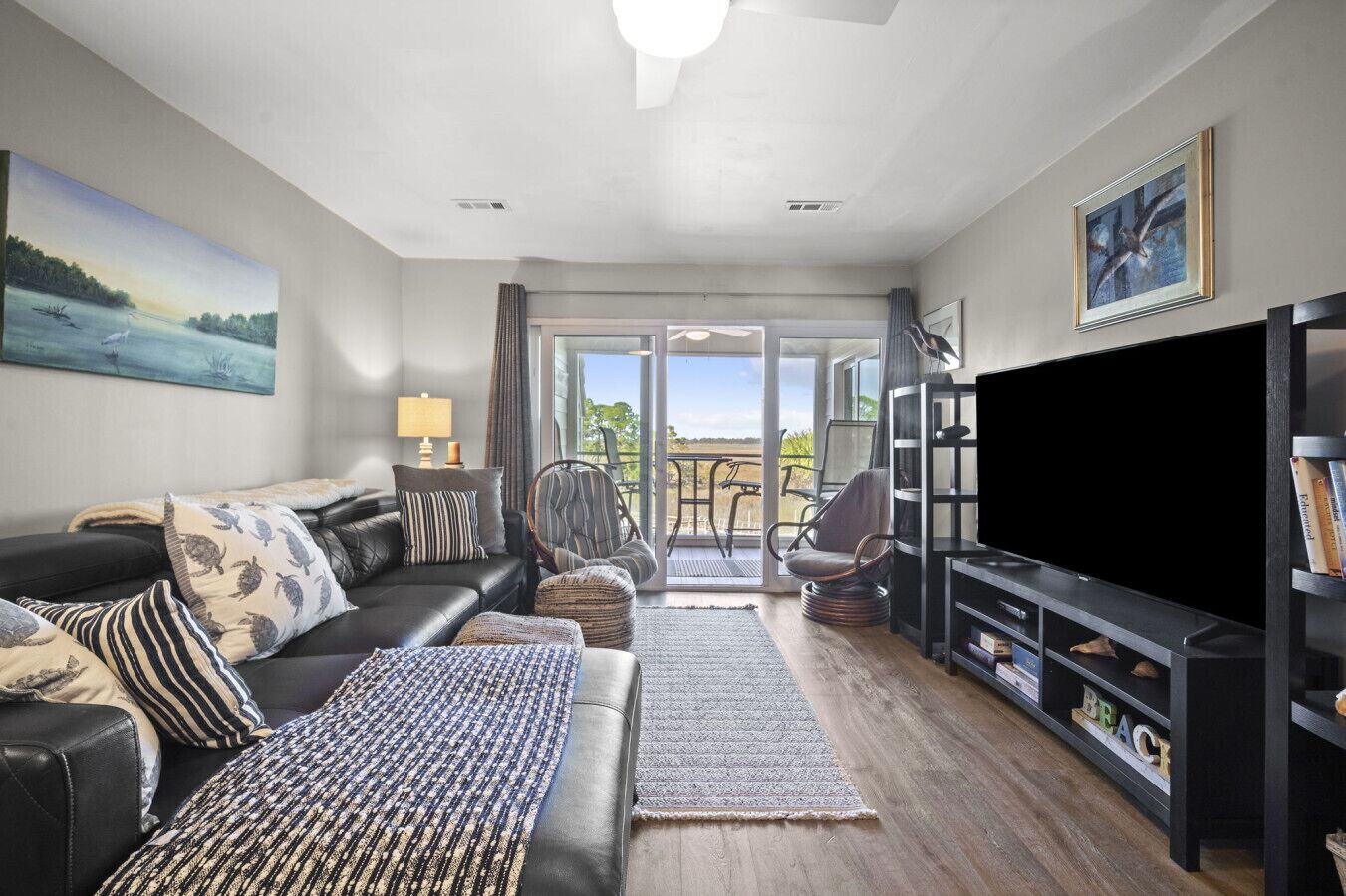 A modern living room with a black leather sofa, striped pillows, a large flat-screen TV, and a bookshelf.