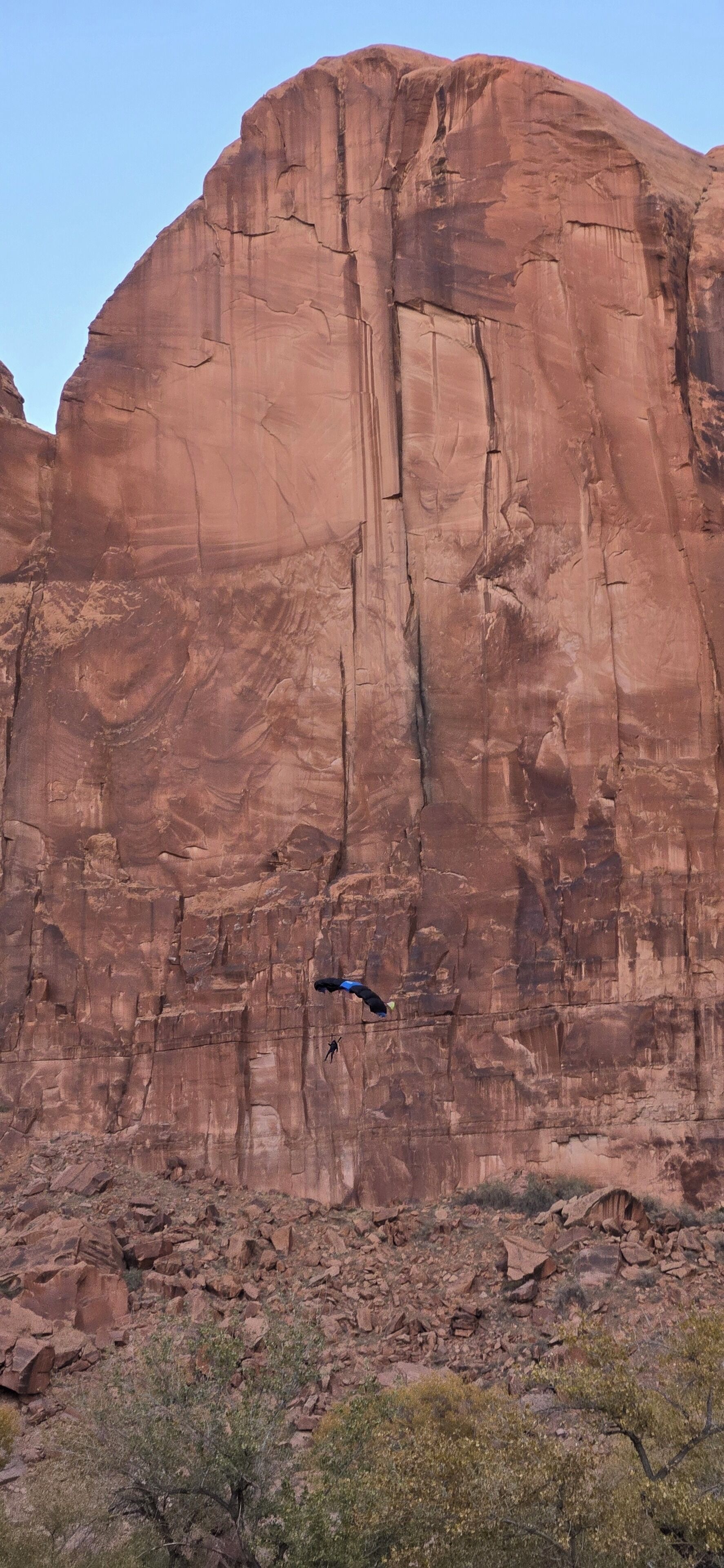 A large red rock formation with a person rappelling down its face.