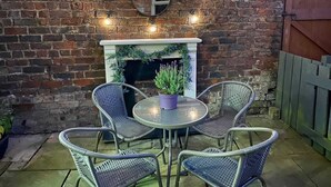 A brick wall with a fireplace, four wicker chairs, and a small table with a potted plant.