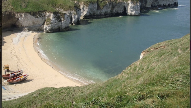 A coastal beach with white cliffs, clear water, and a sandy shore.
