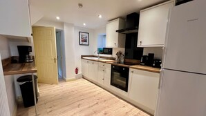 A modern kitchen with white cabinets, a wooden countertop, a black oven, and a white refrigerator.