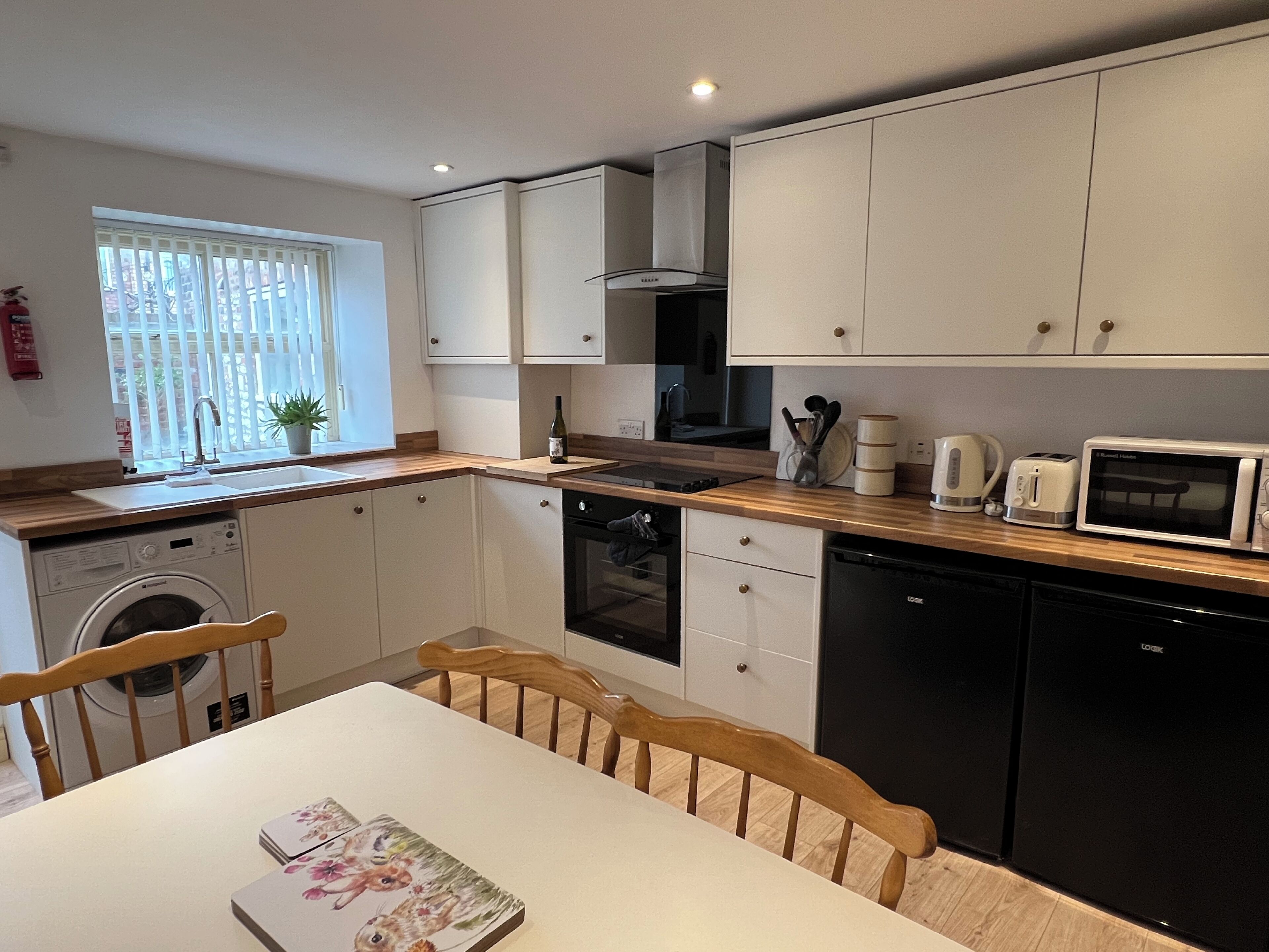 A compact kitchen with a washing machine, dishwasher, microwave, and a small dining area with a table and chairs.