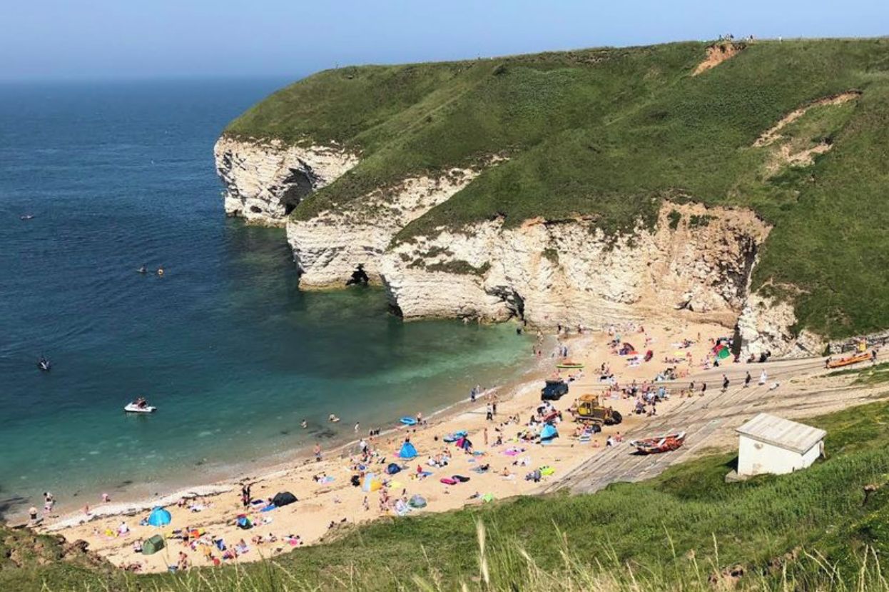 A coastal beach with cliffs, clear waters, and a sandy shore.