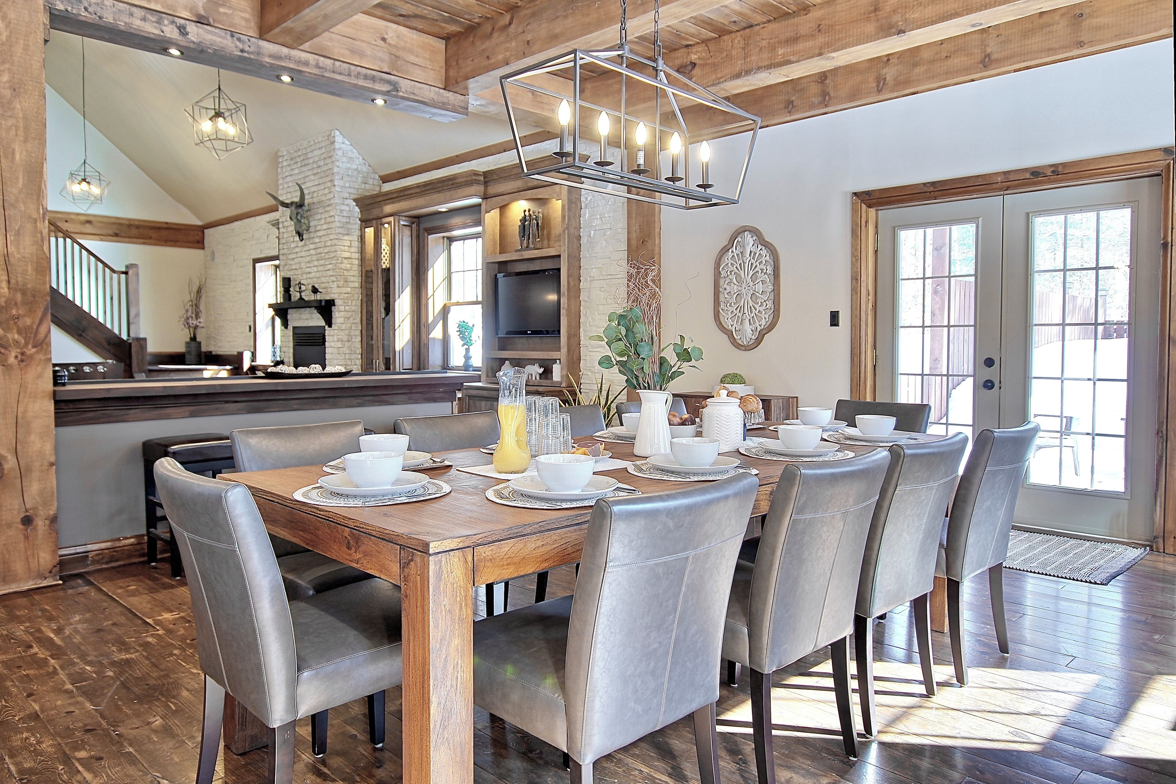 A dining area with a wooden table set for six, surrounded by chairs, a fireplace, and a stone wall.