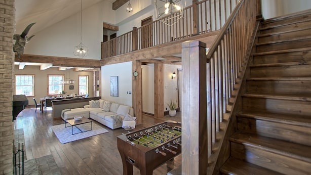 A spacious living area with a high ceiling, wooden staircase, and a foosball table.