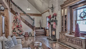A cozy living room with a fireplace, a staircase, and a Christmas tree.