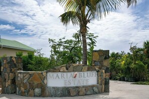 A stone sign with "Maria Bluf Estate" written on it, surrounded by greenery and a palm tree. - Maria Bluff Estate | 7BR Stunning Views |  BookVI (Cruz Bay)