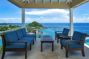 A covered outdoor seating area with a view of the ocean and a distant island. - Maria Bluff Estate | 7BR Stunning Views |  BookVI (Cruz Bay)