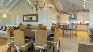 Un comedor espacioso con una gran mesa redonda y sillas de mimbre, un candelabro y una cocina al fondo.