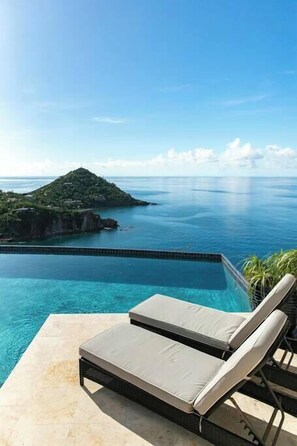 A poolside lounge with a view of the ocean and a distant island. - Maria Bluff Estate | 7-Bedroom Villa | Generator (Cruz Bay)