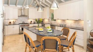Cocina con armarios blancos, una isla central con asientos, iluminación colgante y un salpicadero con diseño de espiga.