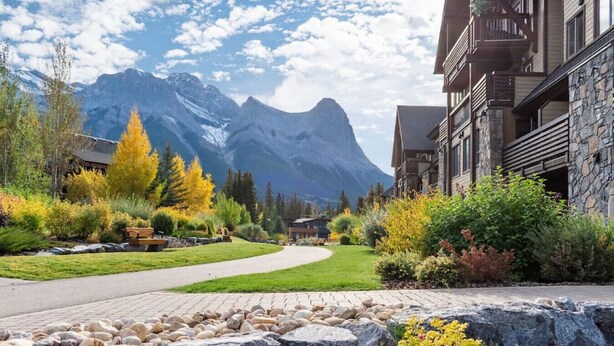 A mountain lodge with a paved walkway, autumn foliage, and a view of a mountain range. - Picturesque Views | Creekside Walking Paths to Town (Canmore)